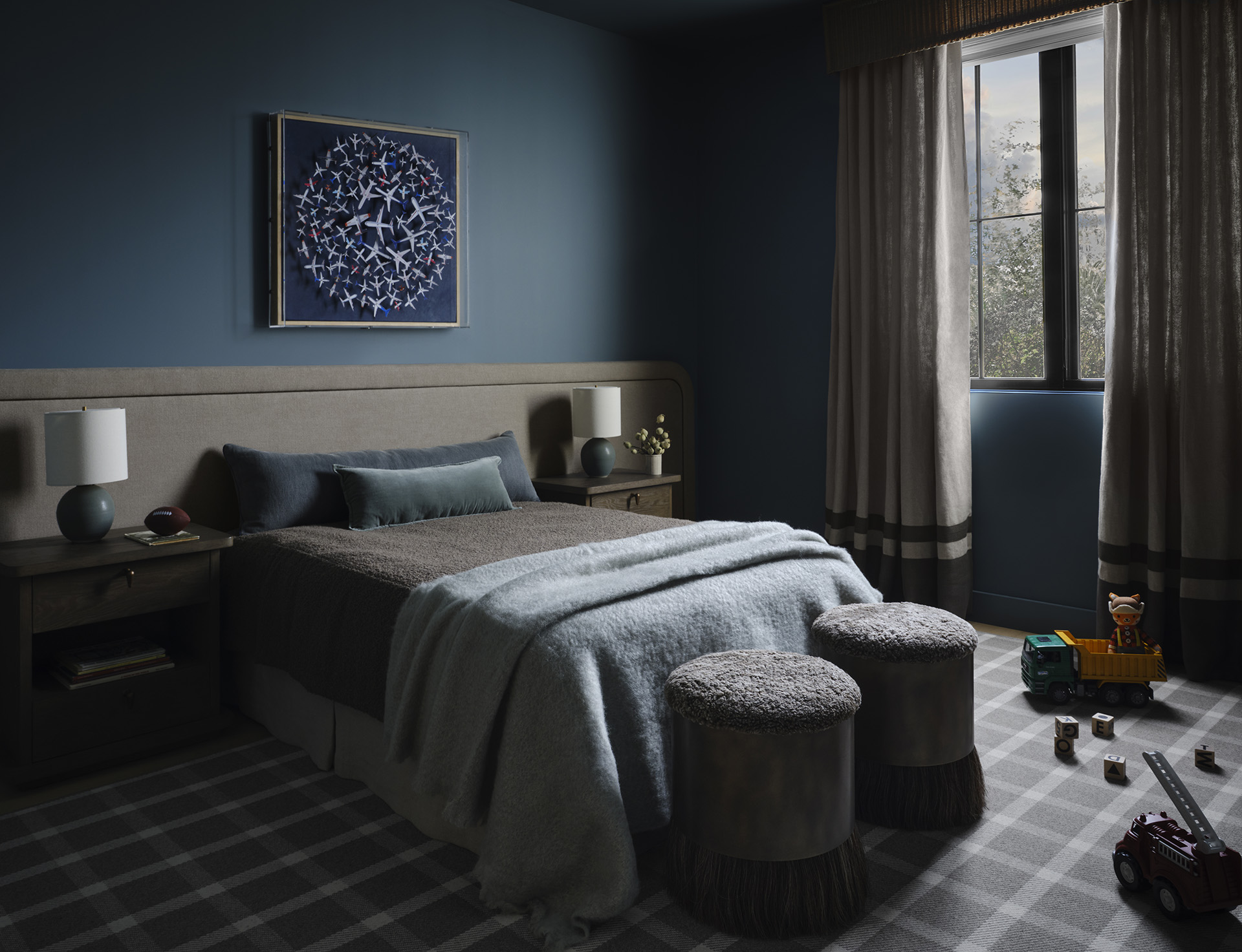 Smoky teal bedroom with upholstered bed, airplane artwork and fringed stools